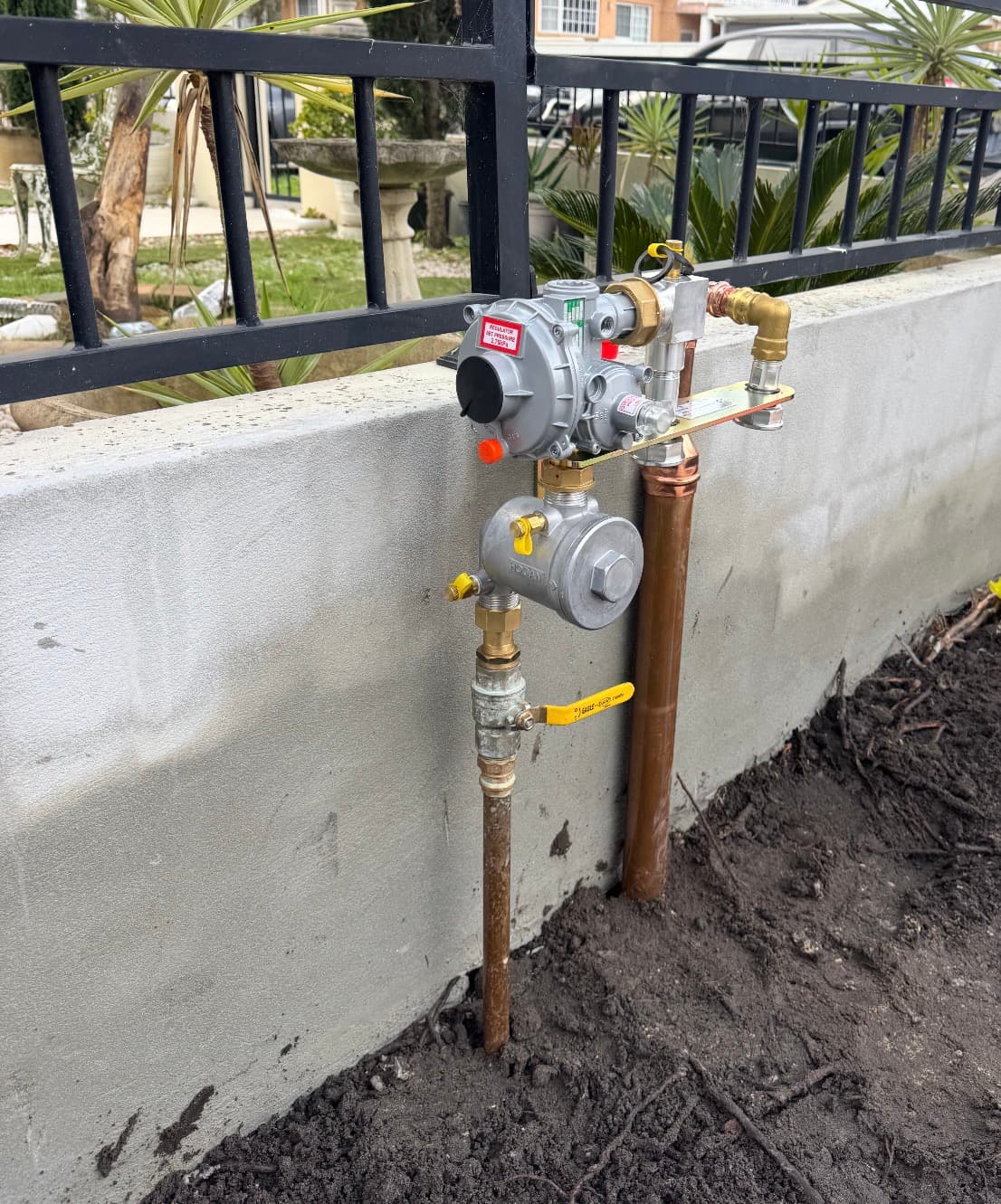 Newly installed gas meter and regulator assembly bracketed to a rendered boundary wall, with copper risers and yellow-handled isolation valves